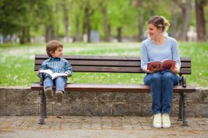 Young woman and cute little boy reading books in a park and talking
